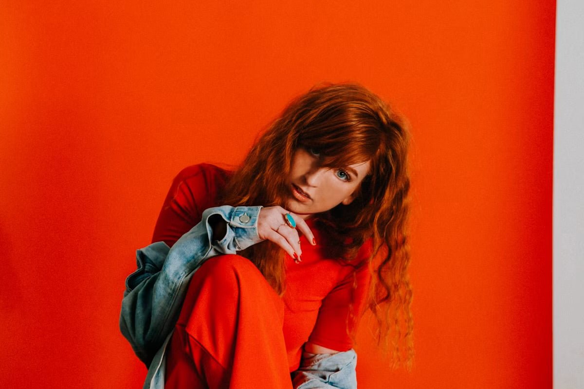 A young woman in vibrant red clothing poses against an orange backdrop, embodying confidence and style.