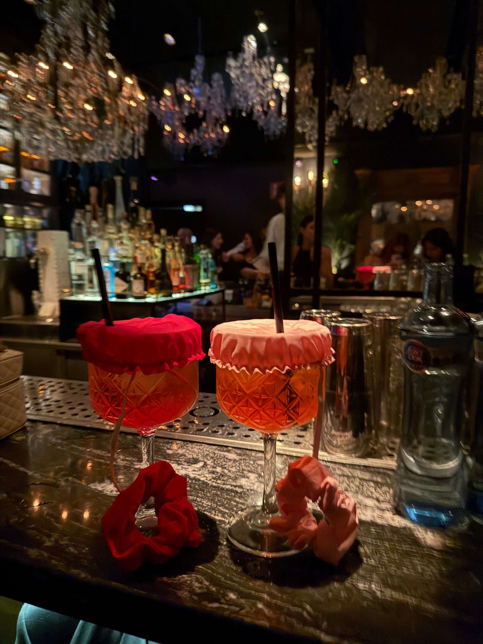 Two cocktails with Noxie™ Safety Scrunchie drink covers on a bar, highlighting stylish anti-drink protection.